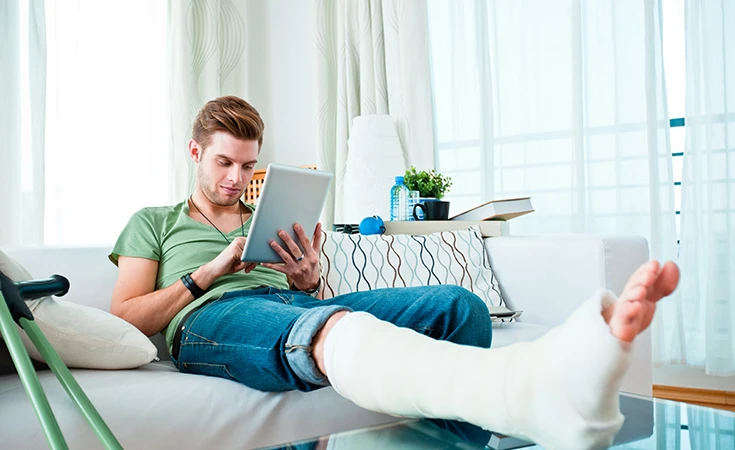 young man working on ipad while elevating foot in a cast