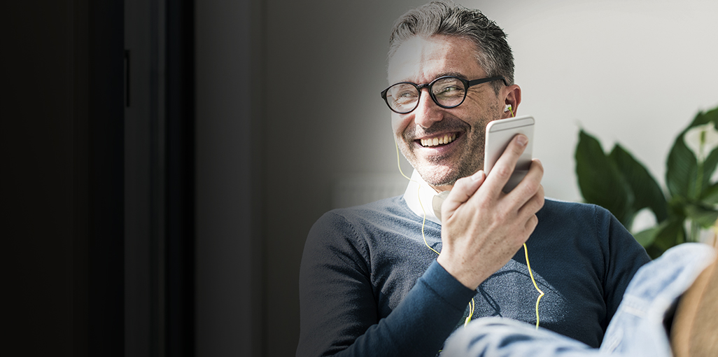 Smiling man relaxing as he listens to a podcast on his mobile device.