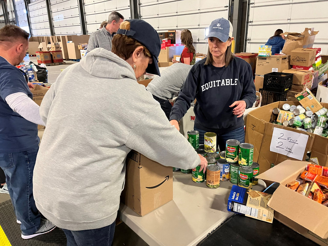 woman wearing an Equitable sweatshirt helping box canned goods
