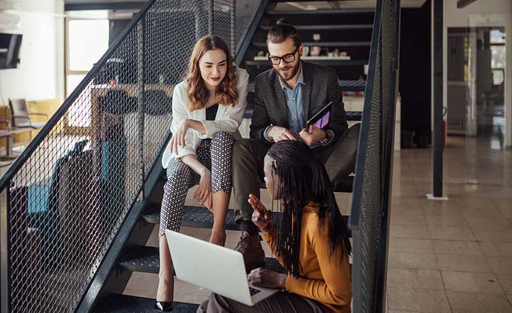  Coworkers discussing something while sitting on stairs.