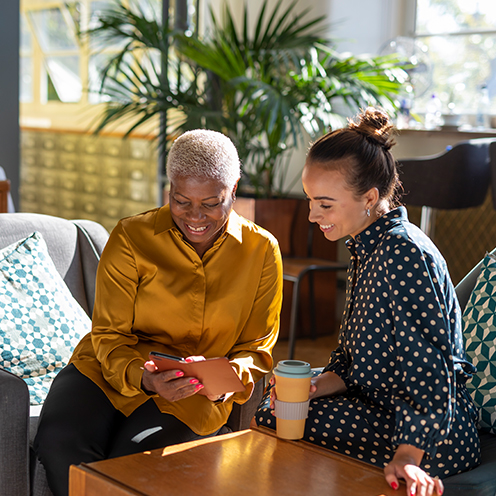 Two women smiling and sharing tablet together