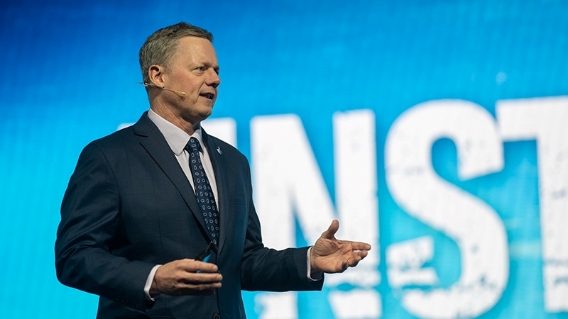 Nick Lane speaking on stage with blue backdrop